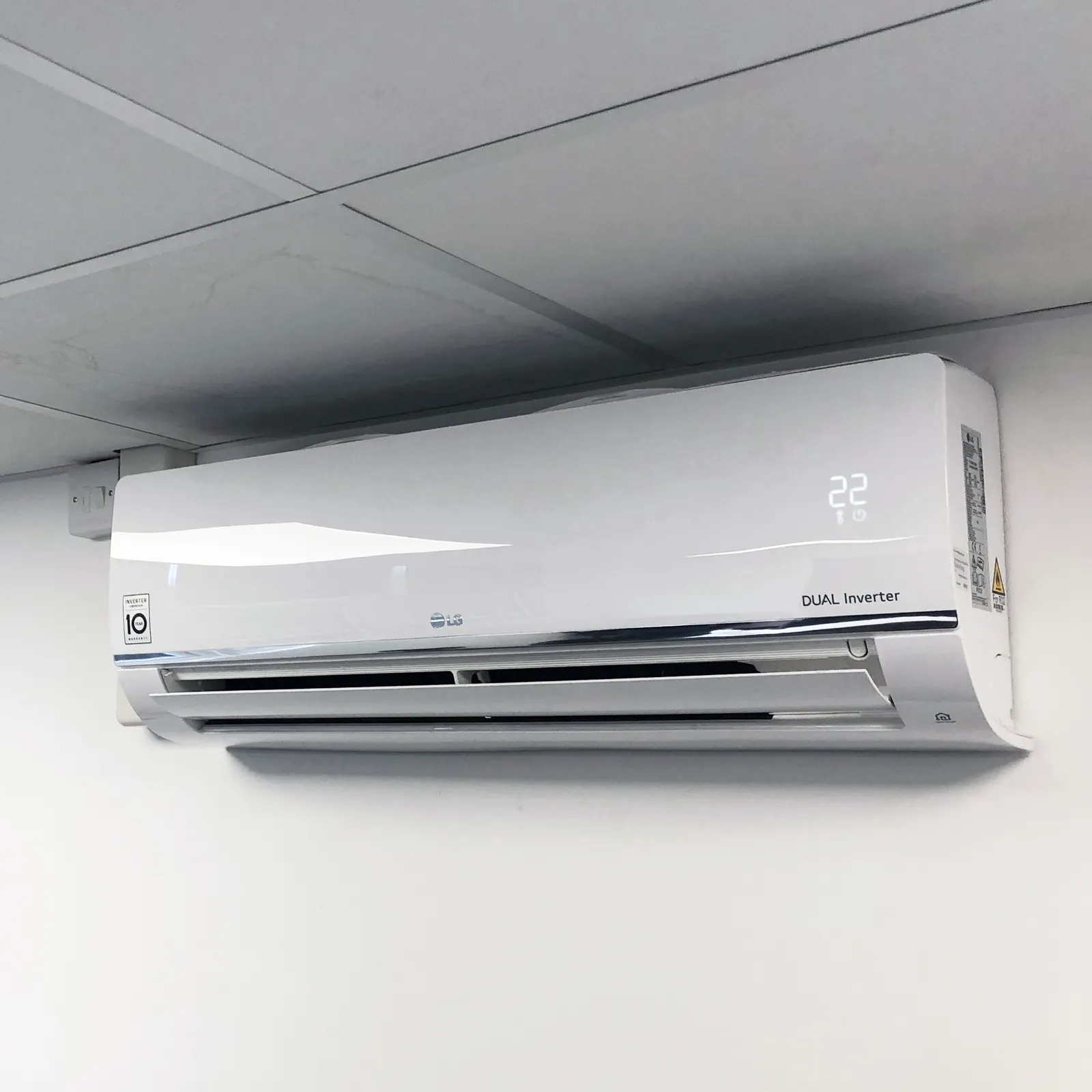 An LG DUAL Inverter wall-mounted split unit installed below a suspended ceiling, its display reading 22°.